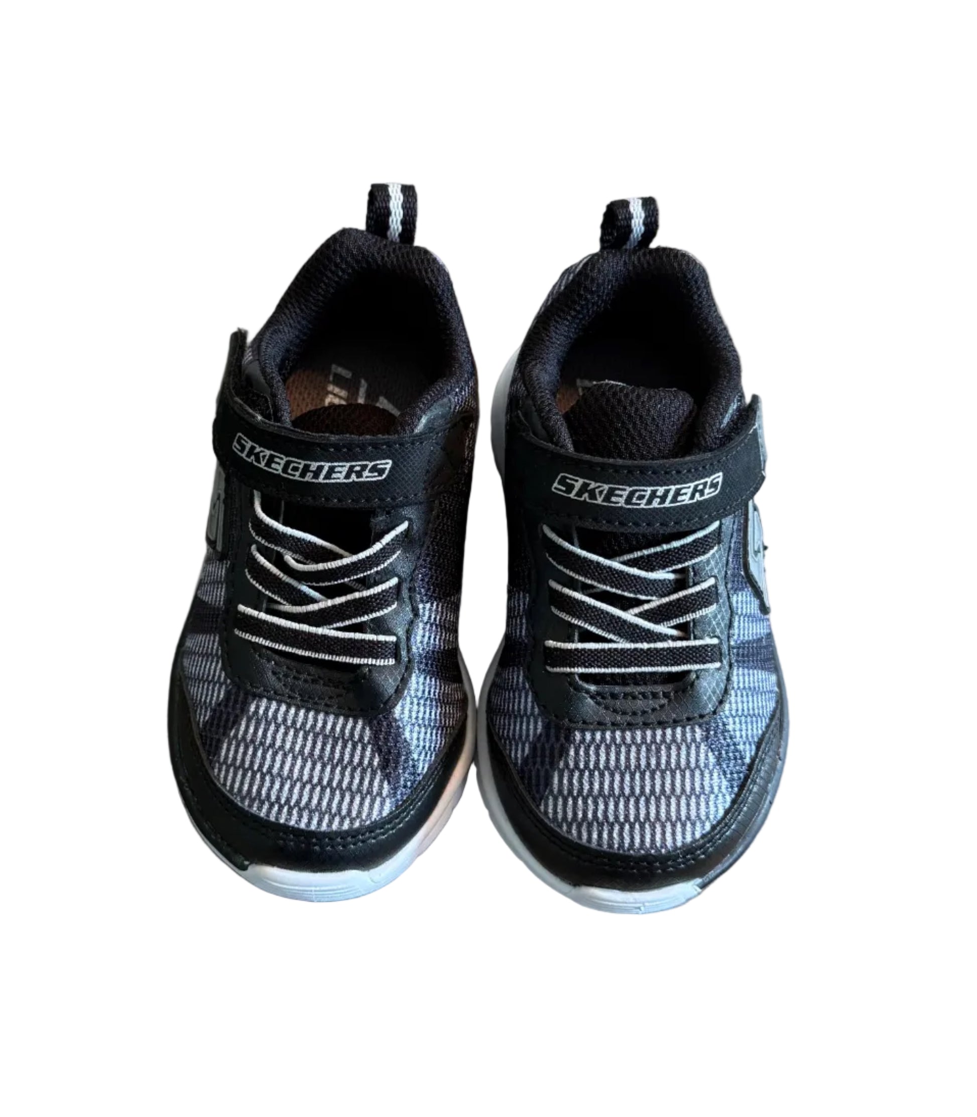 Chaussures de sport Skechers noires en mesh, lacets, semelle claire, logo sur le côté.