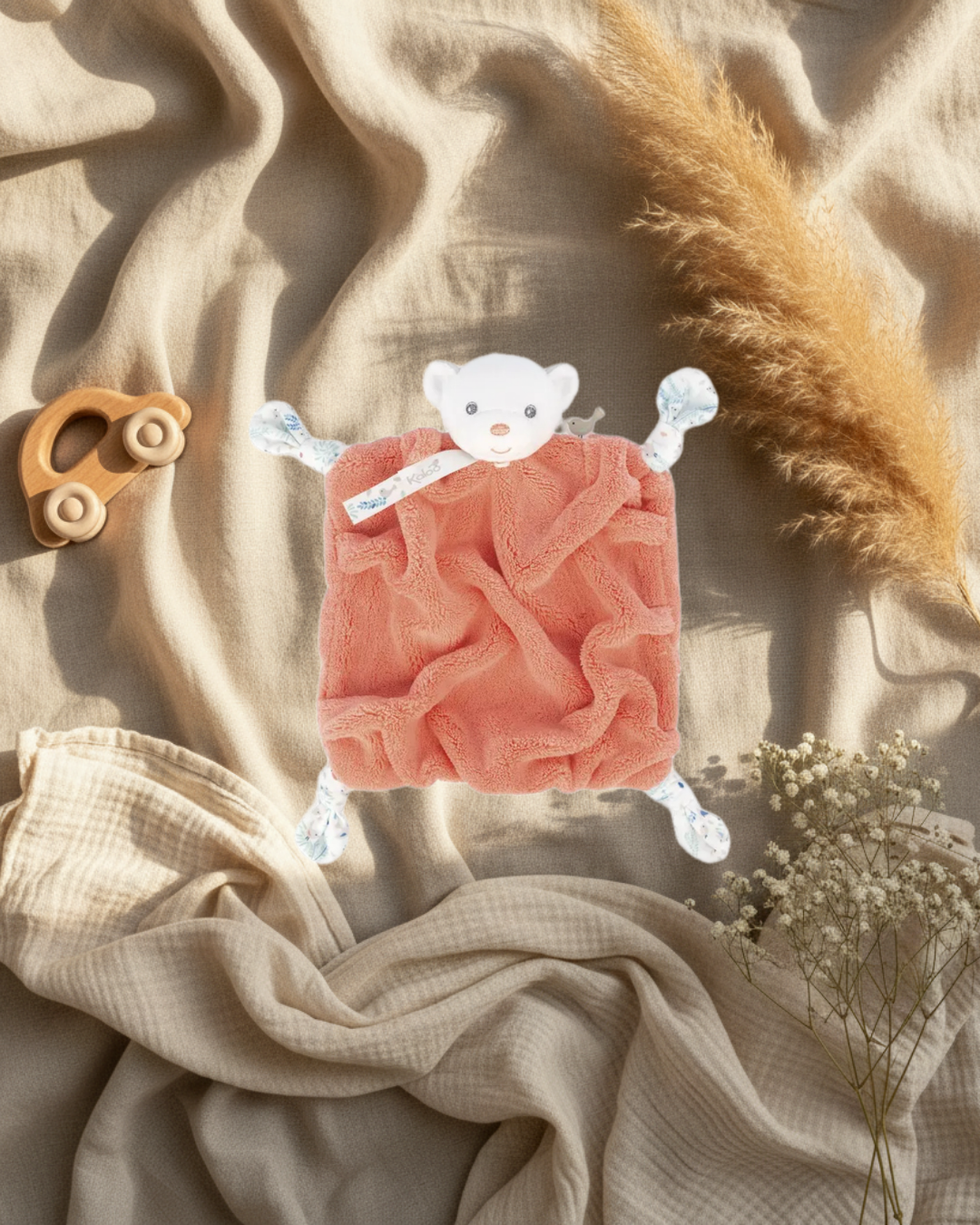 Peluche Kaloo en couleur saumon, visage blanc et petites pattes bleues.