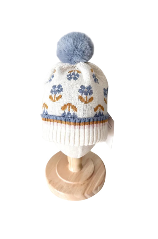 Tuque tricot blanche à motif floral, bord côtelé rayé bleu et jaune, pompon bleu